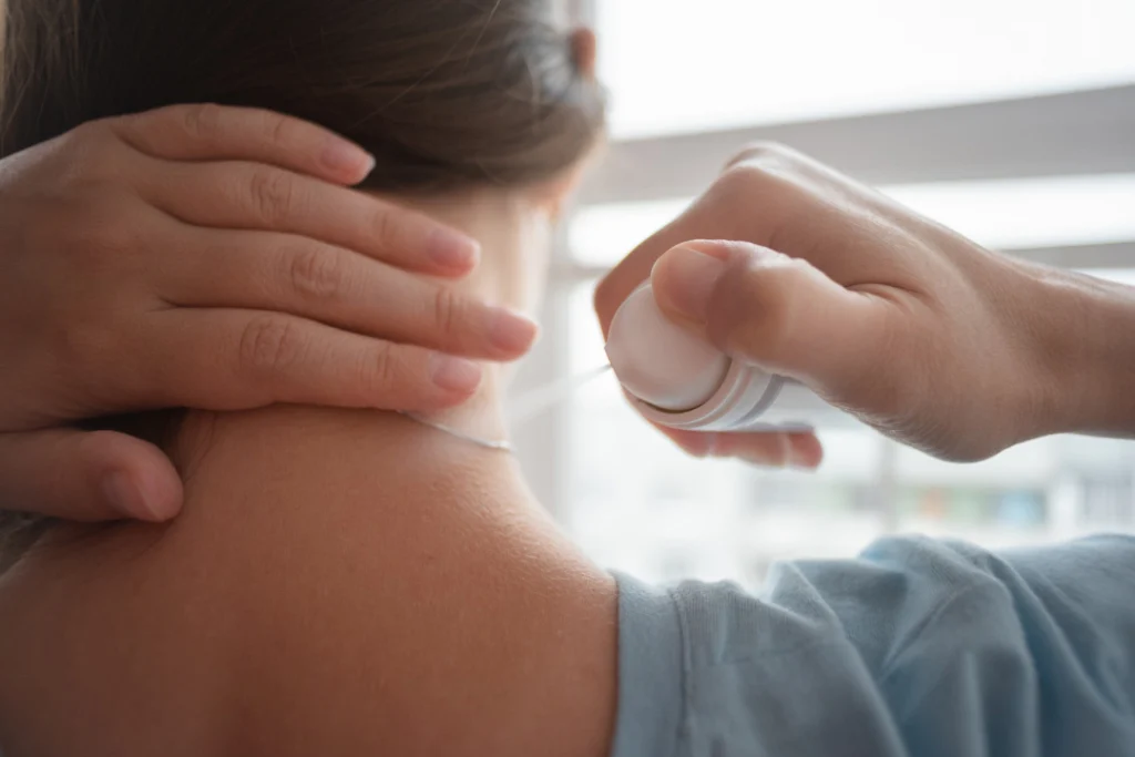 the woman is spraying her neck with the pain relief spray